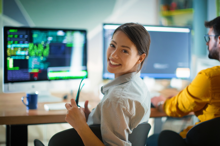 a female full stack engineer smiling with a coding screen in the background