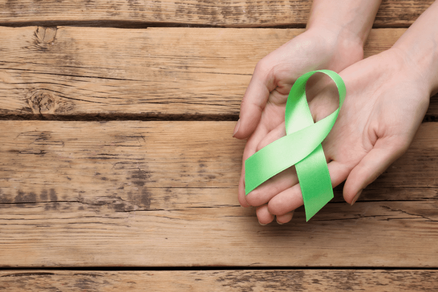 woman holding a green ribbon, the symbol of mental health awareness, on her hands