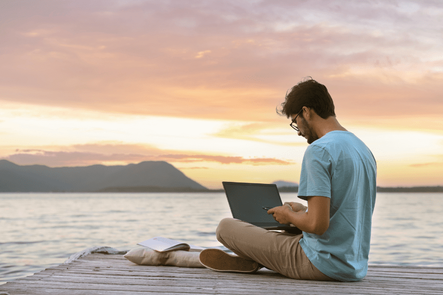 a digital nomad working on a laptop sitting by the sea