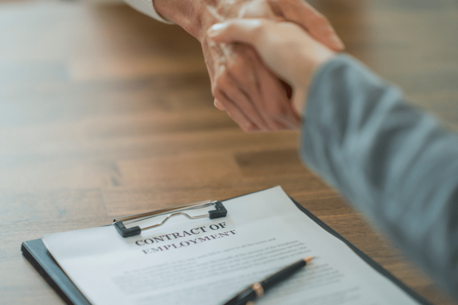 Employer and Employee shaking hands with employment contract lying on the table