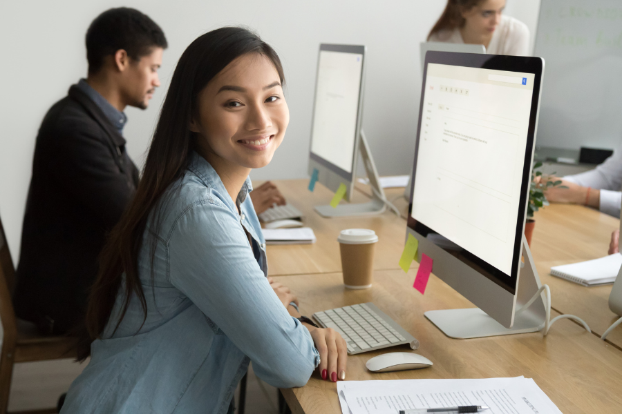 an Asian female employee smiling and looking at camera in front of a computer