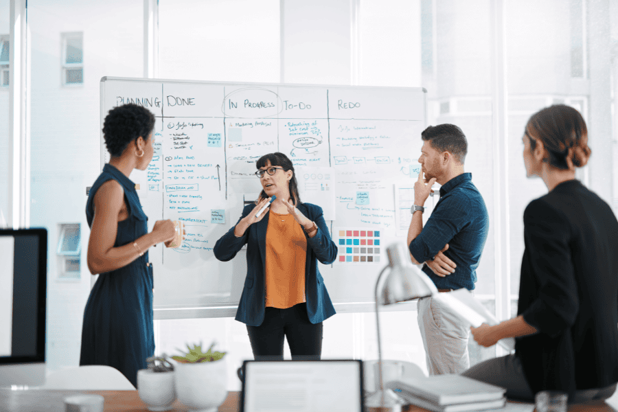 four colleagues discussing strategies in front of a white board