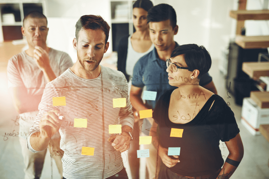 Group of startup business owners discussing IC compliance using sticky notes on Glass door