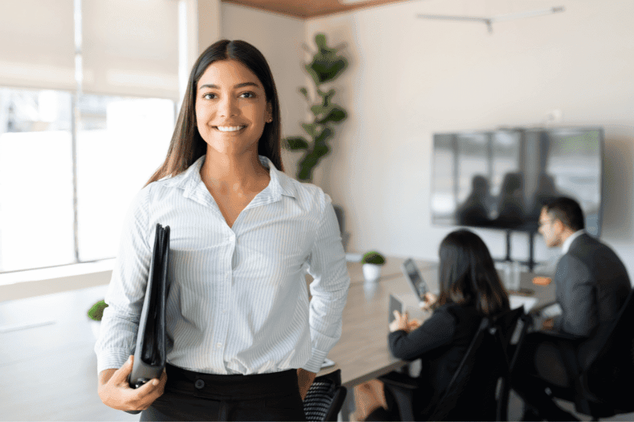 Hispanic businesswoman standing in a meeting room with colleagues discussing in the background