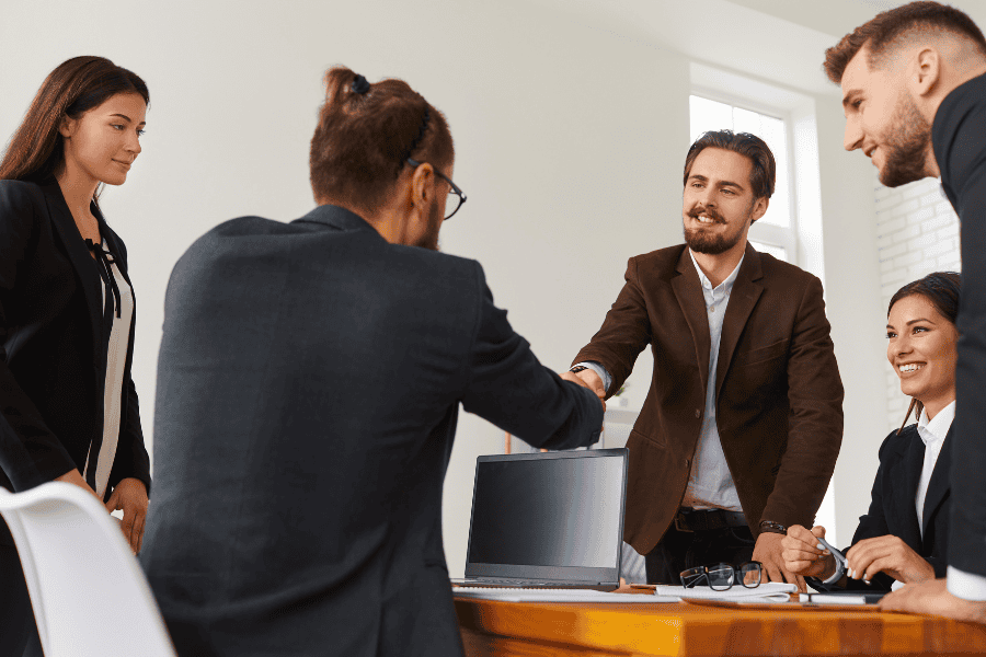 two businessmen shaking hands next to three colleagues