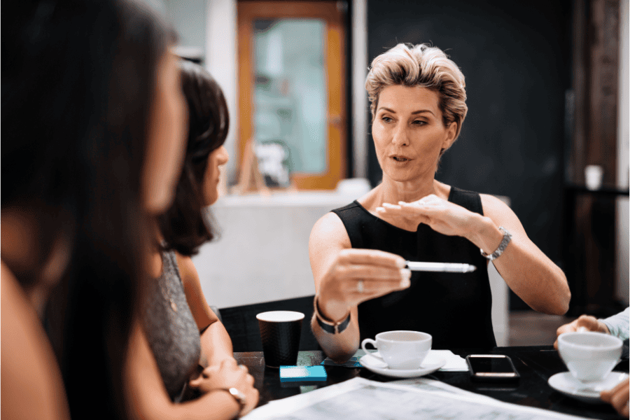a woman in a business meeting, holding a pen while presenting ideas to colleagues at a table