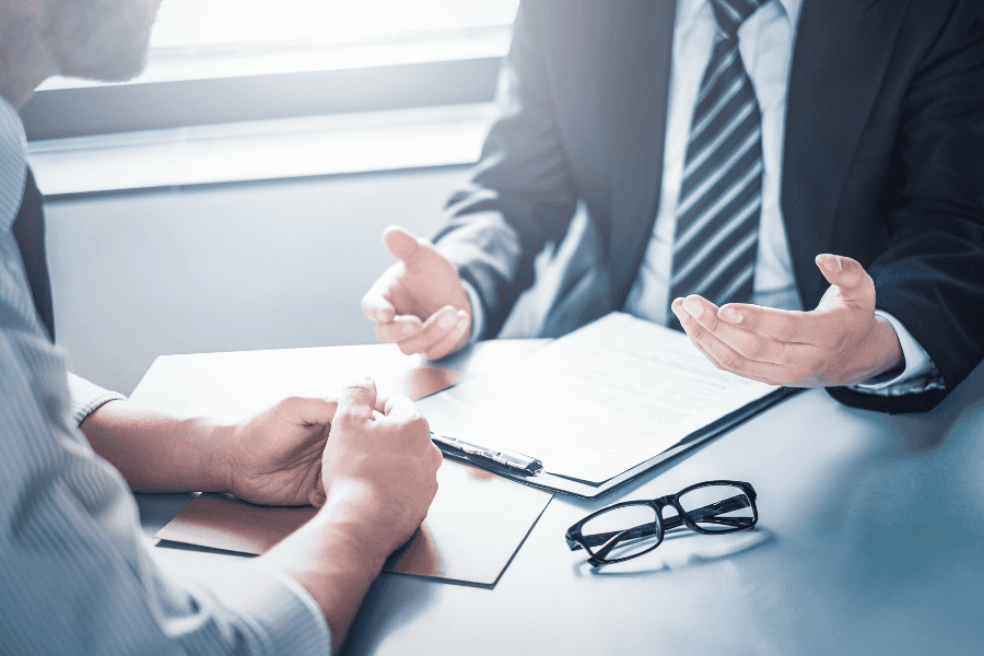 two colleagues having a conversation across a table with a clipboard and glasses on it