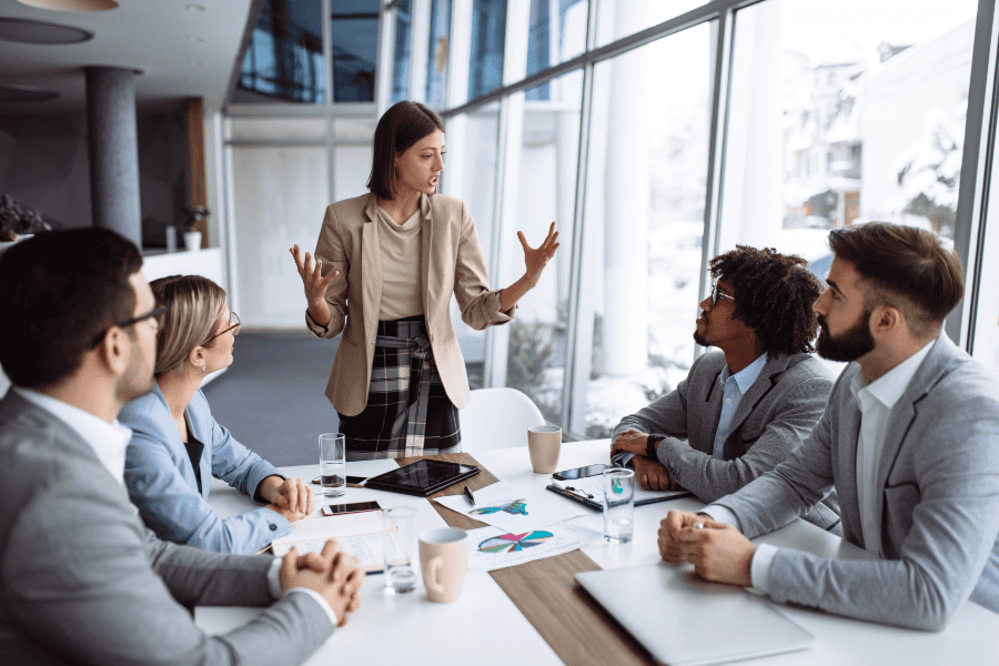 a woman in a blazer leading a discussion with four colleagues in an office