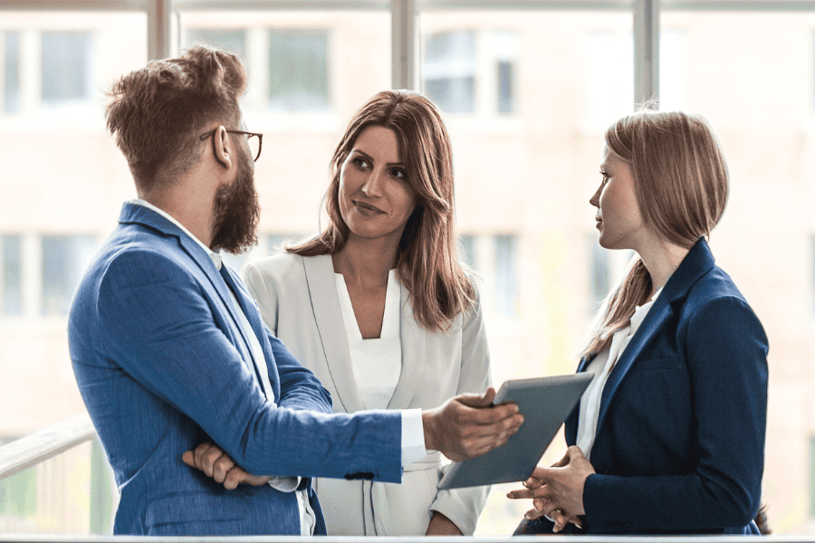 Three business professionals in suits discussing work in a modern office.