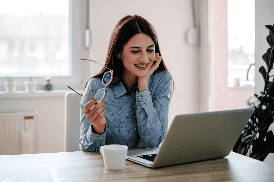 an independent contractor smiling and looking at a laptop while holding a pair of glasses