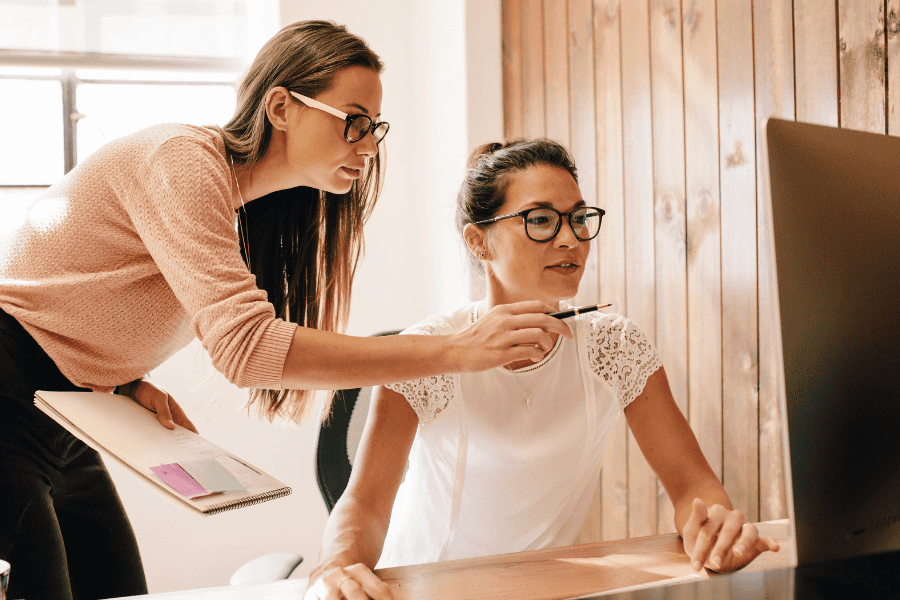 two female colleagues working in front of a monitor with one pointing at it