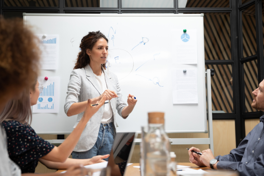 a professional woman leads a market selection discussion in front of a whiteboard while colleagues observe