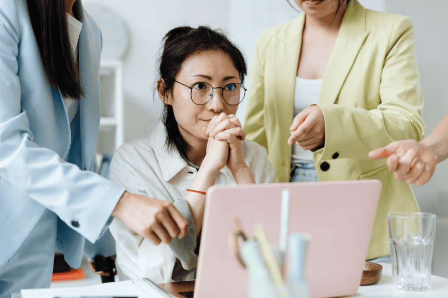 a professional woman contemplating in front of a laptop with two colleagues on the side
