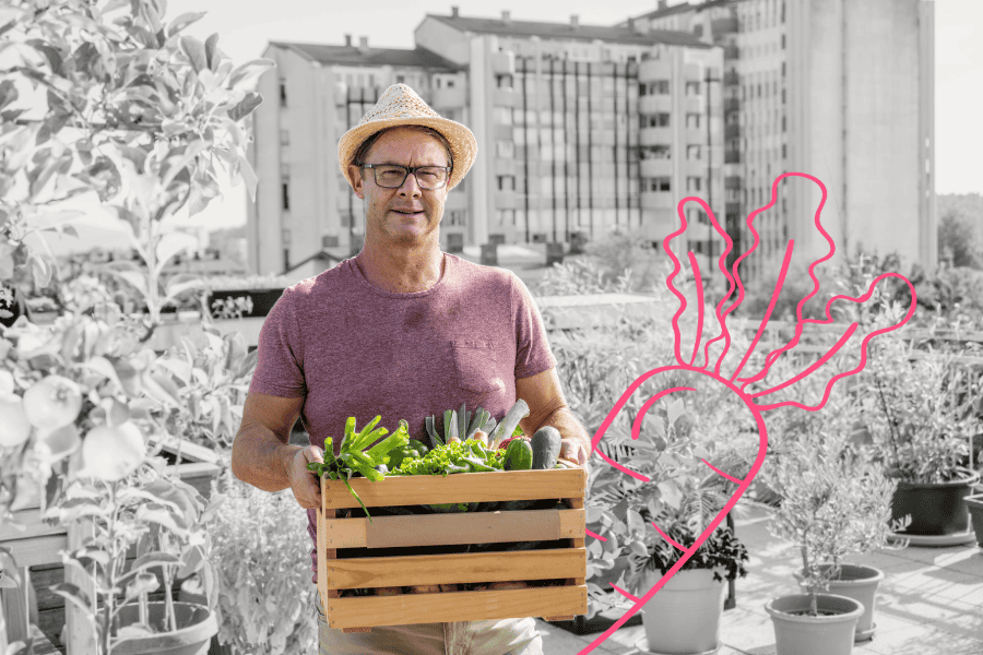 A man holds a wooden crate of fresh green vegetables in a rooftop garden.