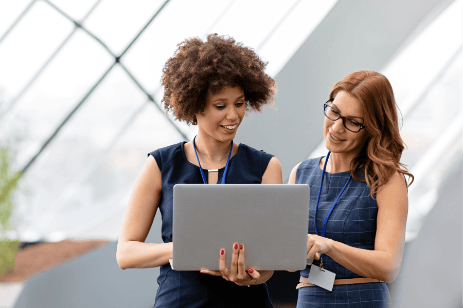 Two professional women reviewing ultimate beneficial ownership compliance requirement on a laptop.