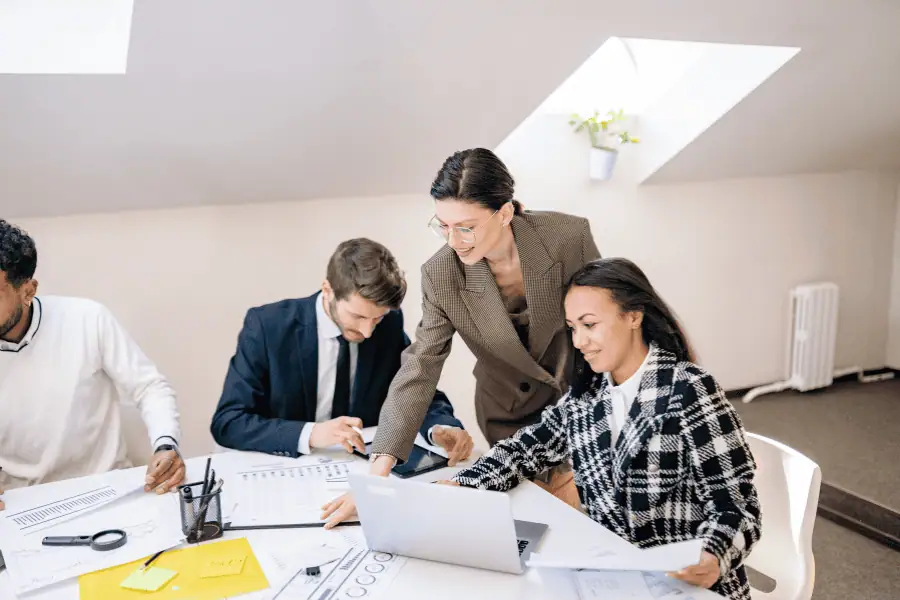 Team of professionals collaborating around a laptop in a bright attic office.