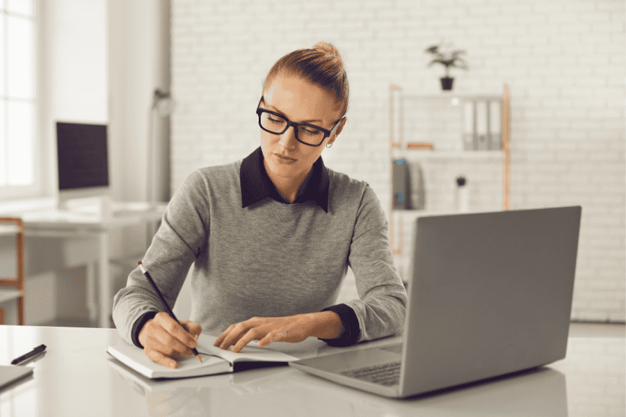 Woman working on remote work policy at her desk with laptop and notebook.